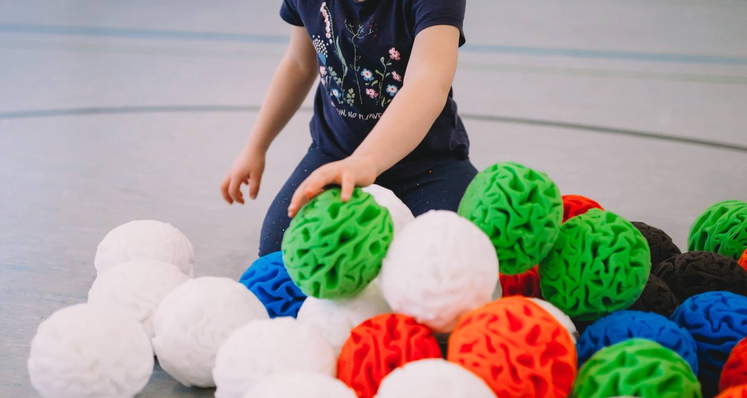 A toddler reaching for a green snowball in a pile of colourful balls