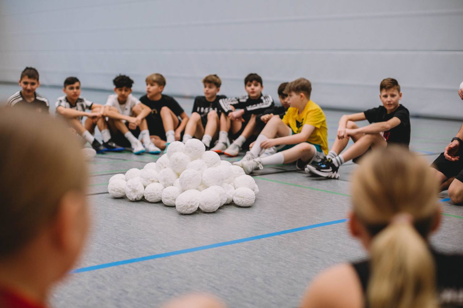 A school class sitting around a pile of white snowballs in the gym