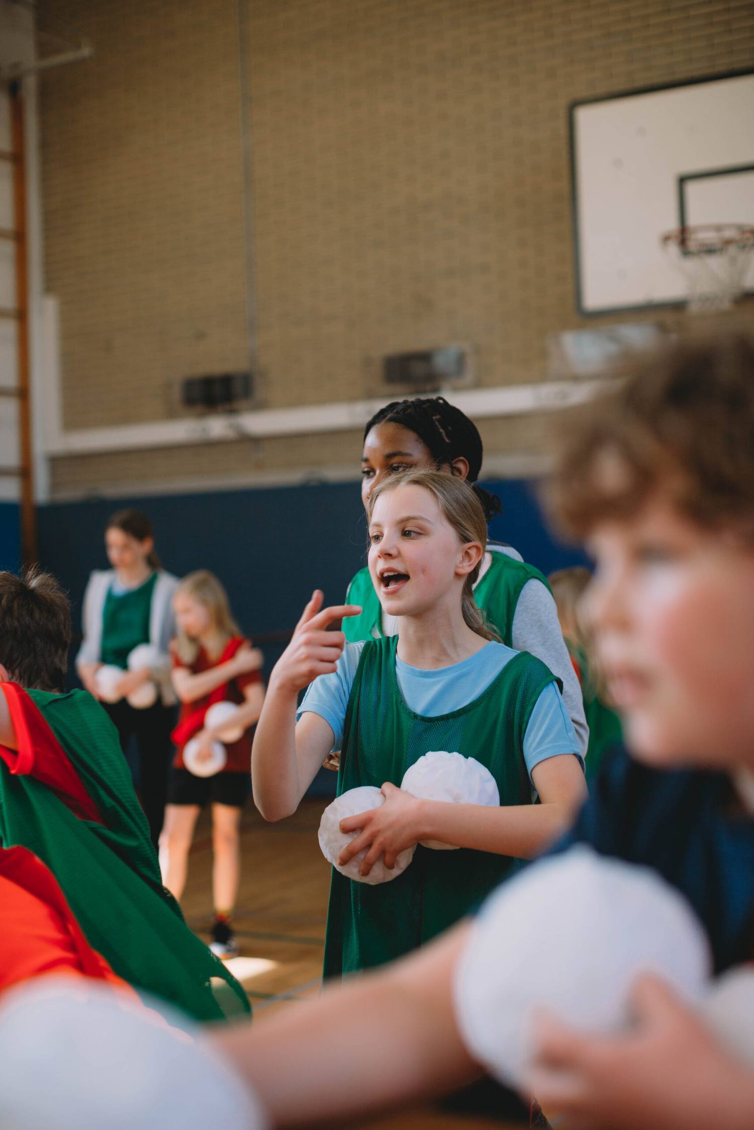 Children in green bibs playing with snowballs at a sports club
